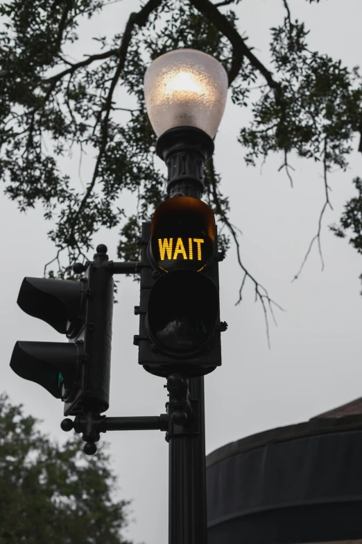 a traffic light with an illuminated yellow sign that reads wait