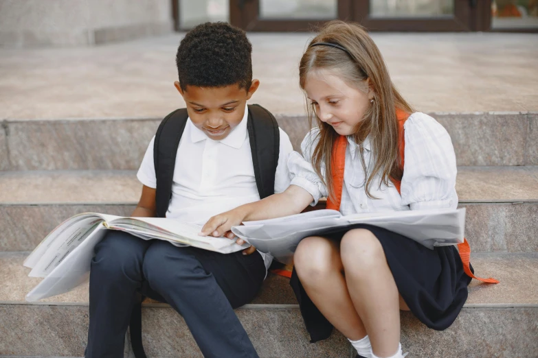 two students are sitting on steps and reading papers