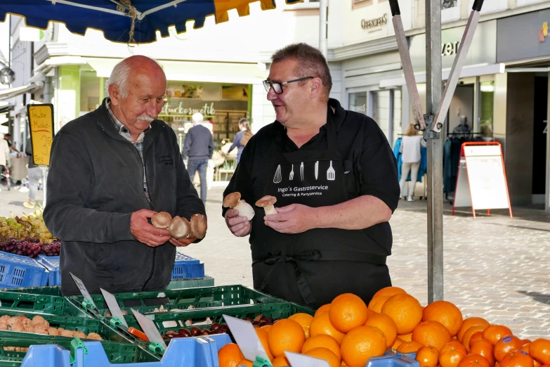 two people standing by an outdoor market area with oranges