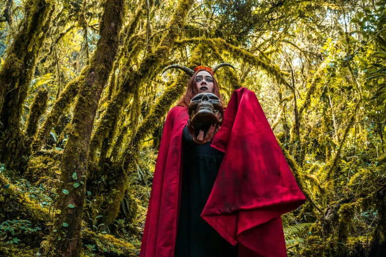 a man is dressed in red cloak standing in a forest