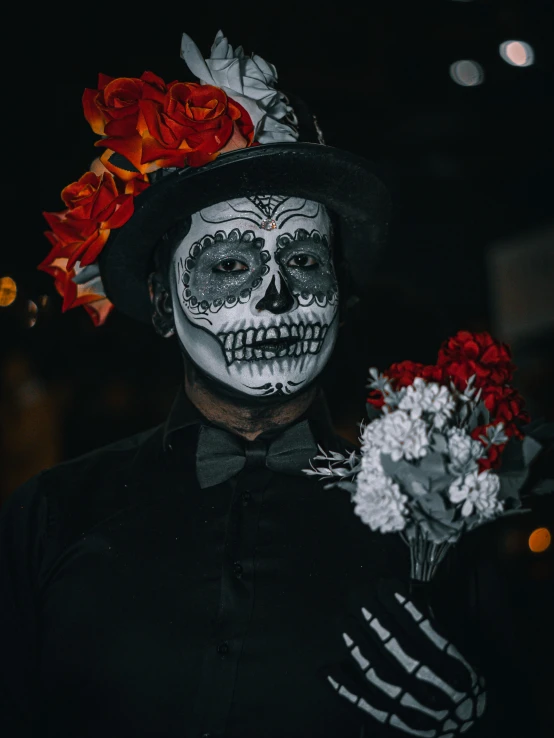 a man wearing a skeleton outfit, black hat and red flowers