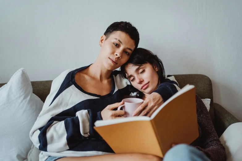 a man and woman are laying on a couch, reading books