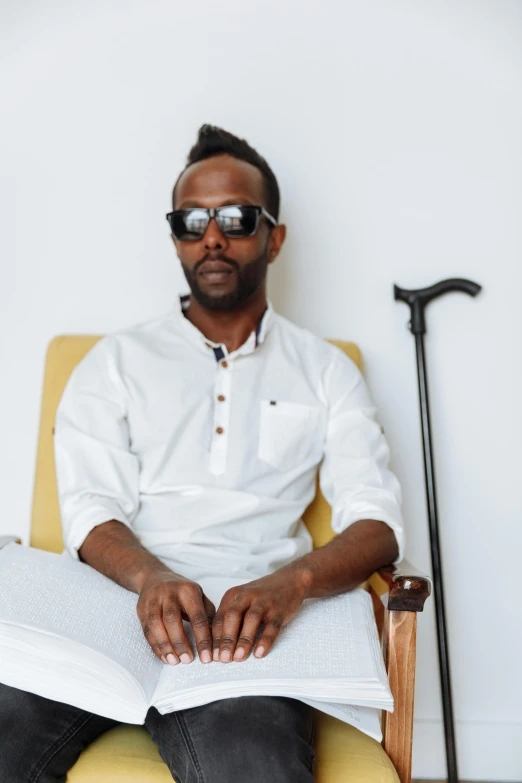 the man sits in a chair wearing sunglasses while reading a book