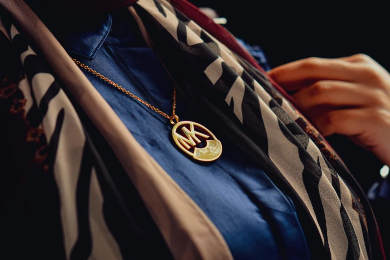 the golden initial pendant is mounted on a striped shirt