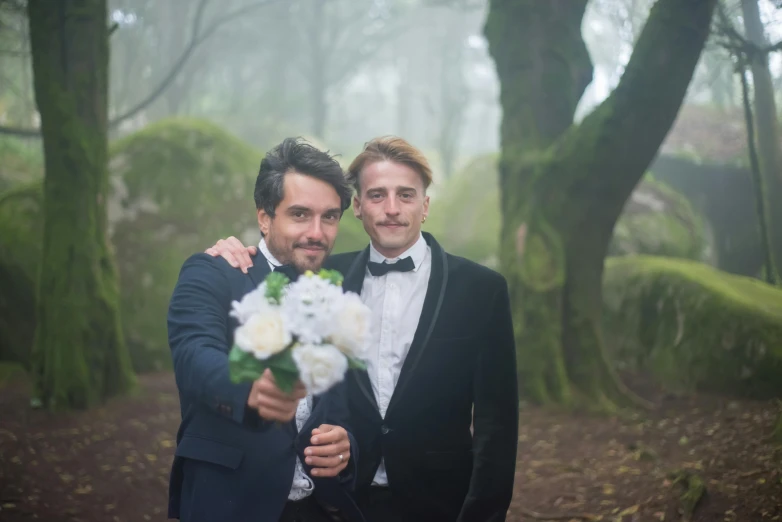 two men in formal clothes with flowers hugging each other