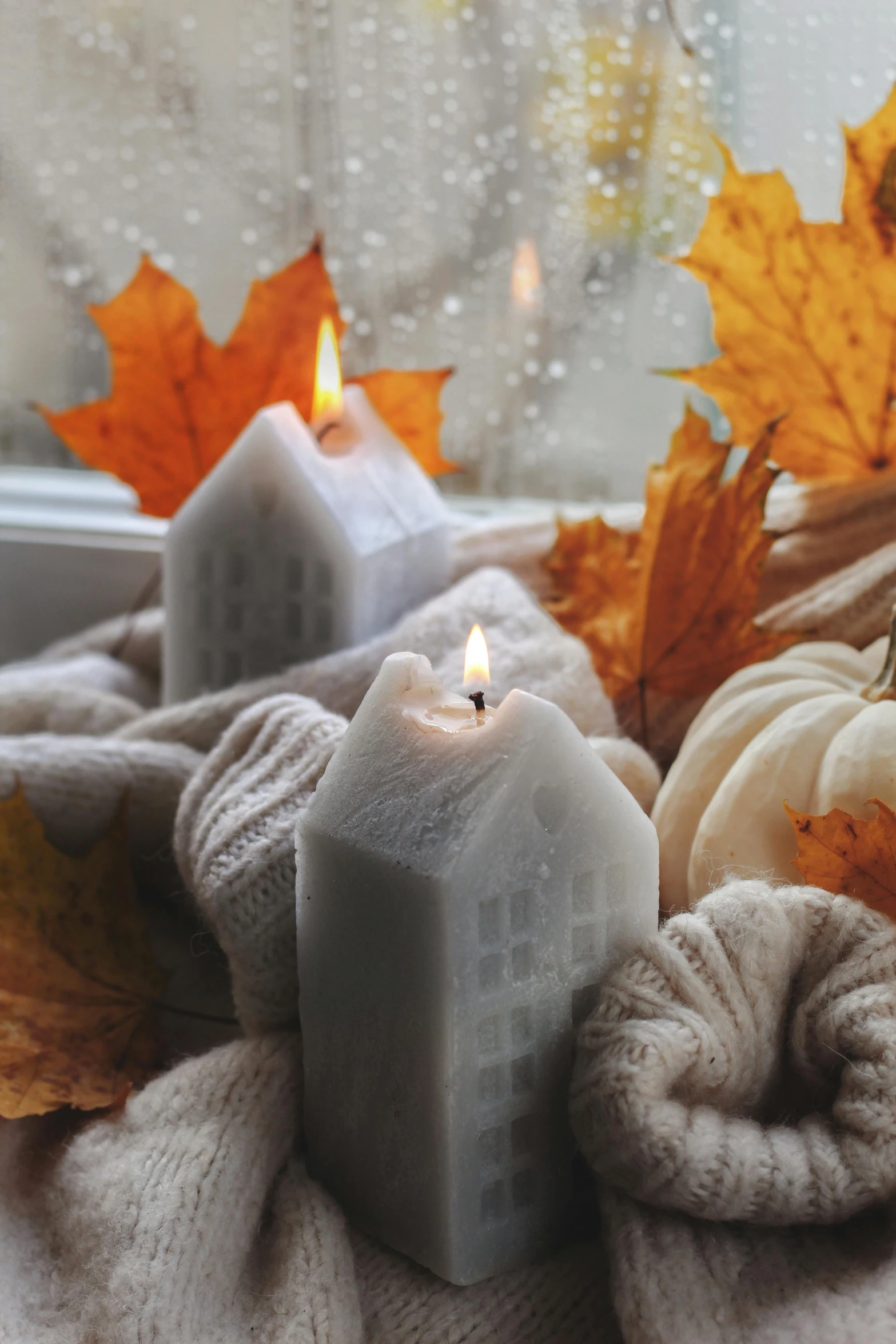 two candles lit on white fabric next to autumn leaves