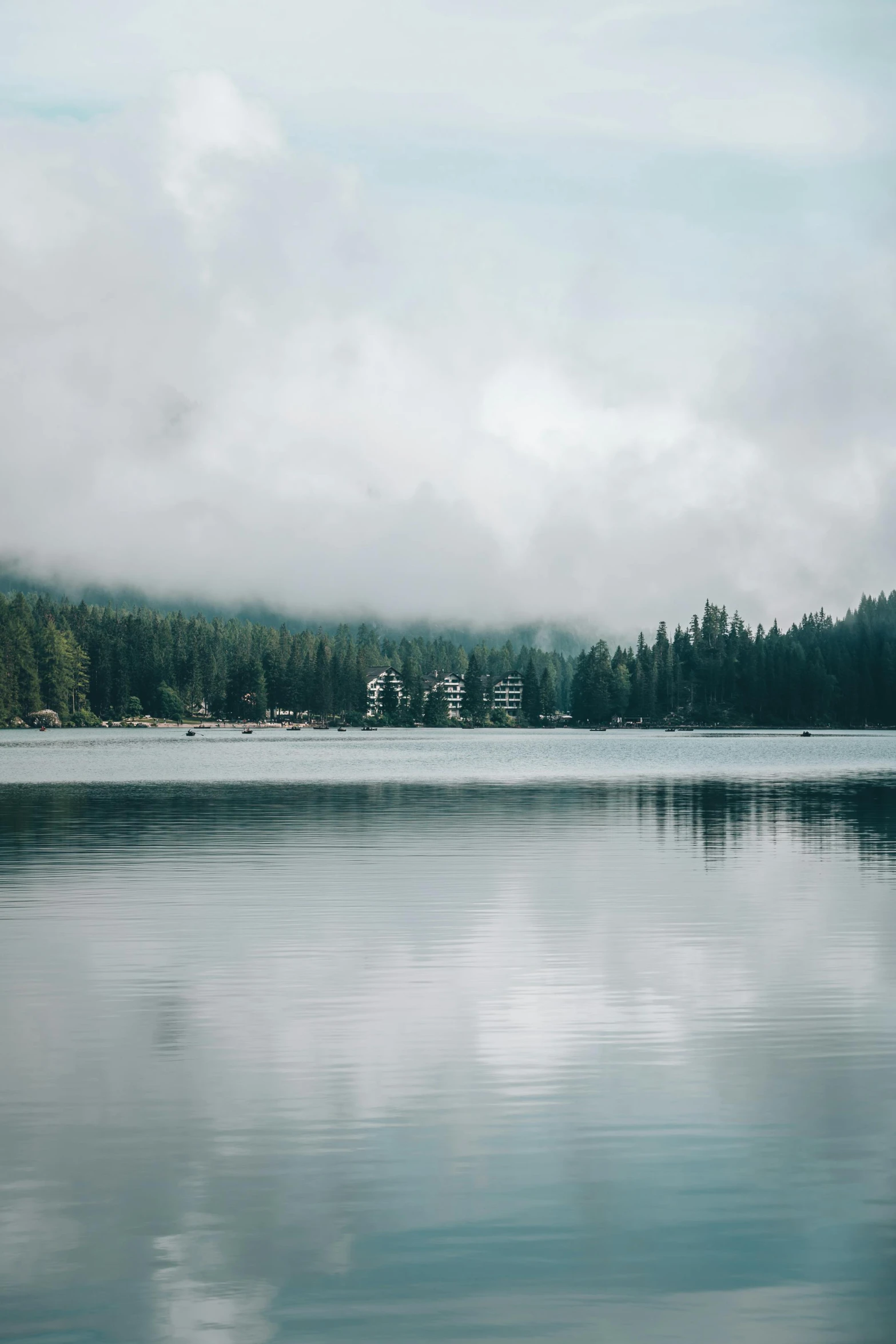 clouds are hanging over the water near a forest