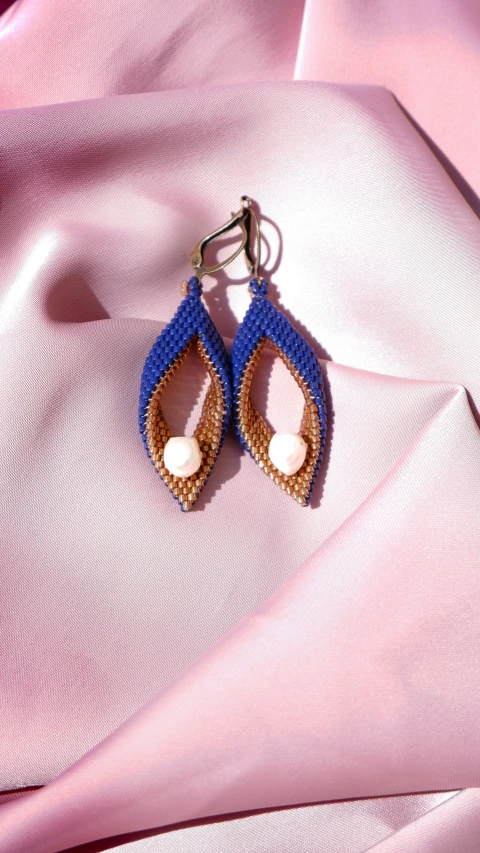 a pair of earrings sitting on top of pink fabric