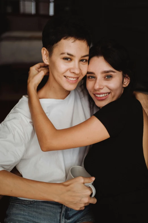 a smiling girl is hugging a younger girl with her arm around her