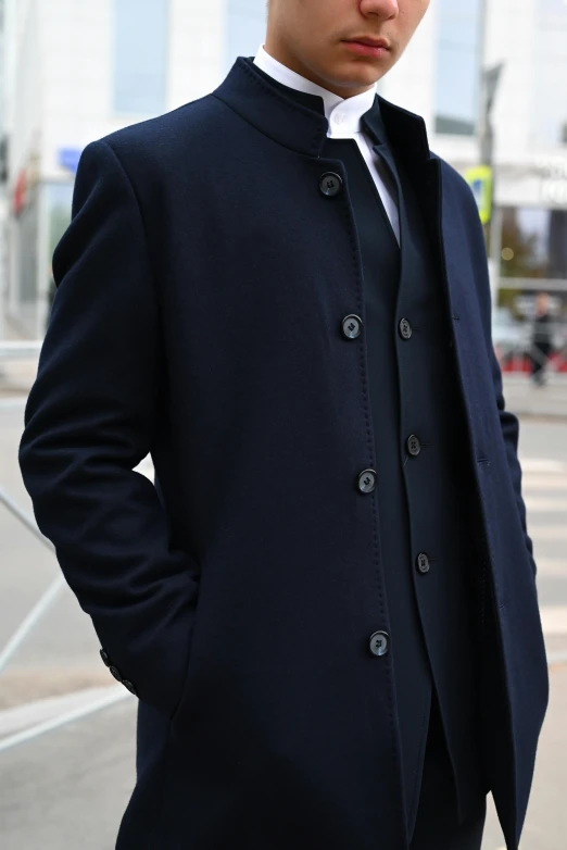 a man in a black coat standing next to some tall buildings