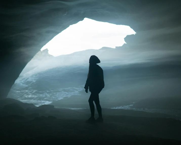 the person in a dark coat is standing inside a cave