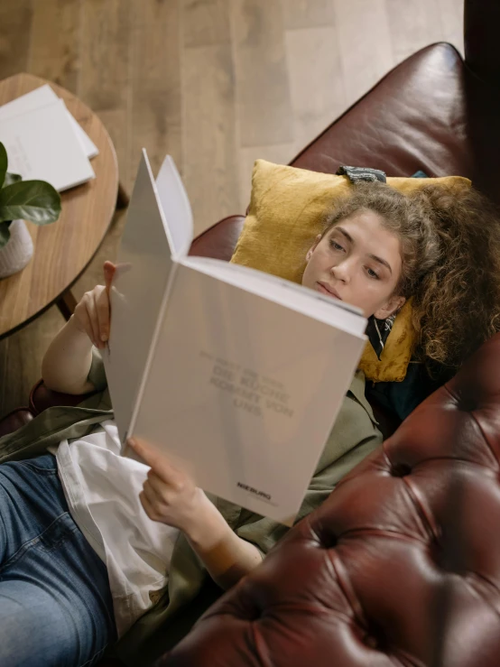 a girl laying on a couch with an open book
