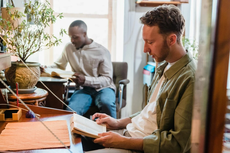 two men are sitting at a table reading the bible