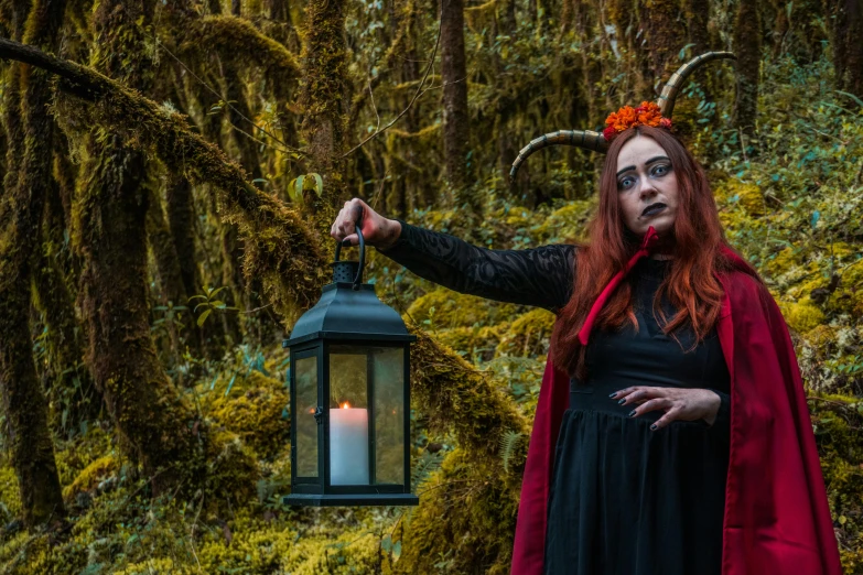 a woman in a black dress with horns and a red cape is holding a lantern