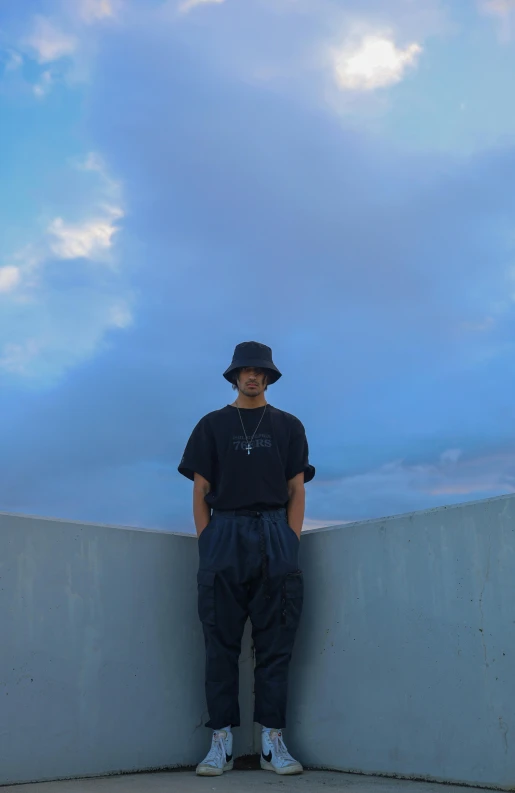 a person stands against a wall wearing a hat and a tshirt