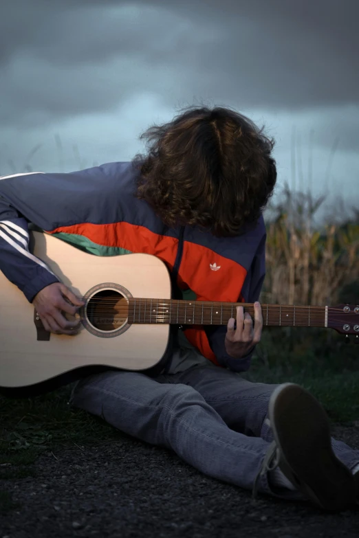 a person with an acoustic guitar sitting on the ground