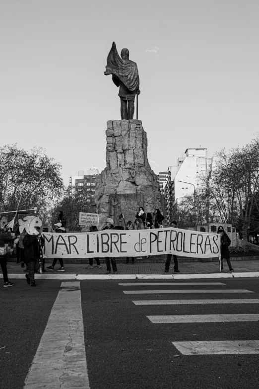 people in a city street holding a banner with a statue behind it