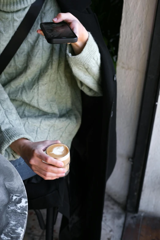 the woman holds her cup of coffee and uses the phone