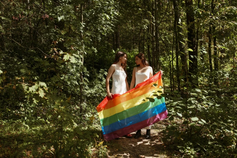 two women standing holding a rainbow flag in the forest