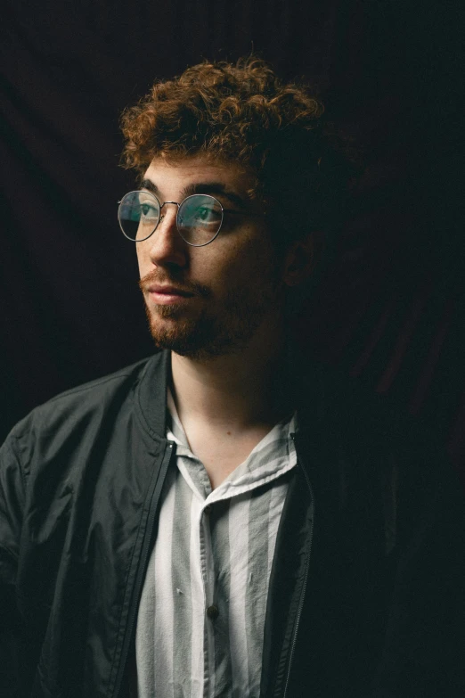 a man with round glasses standing in the dark