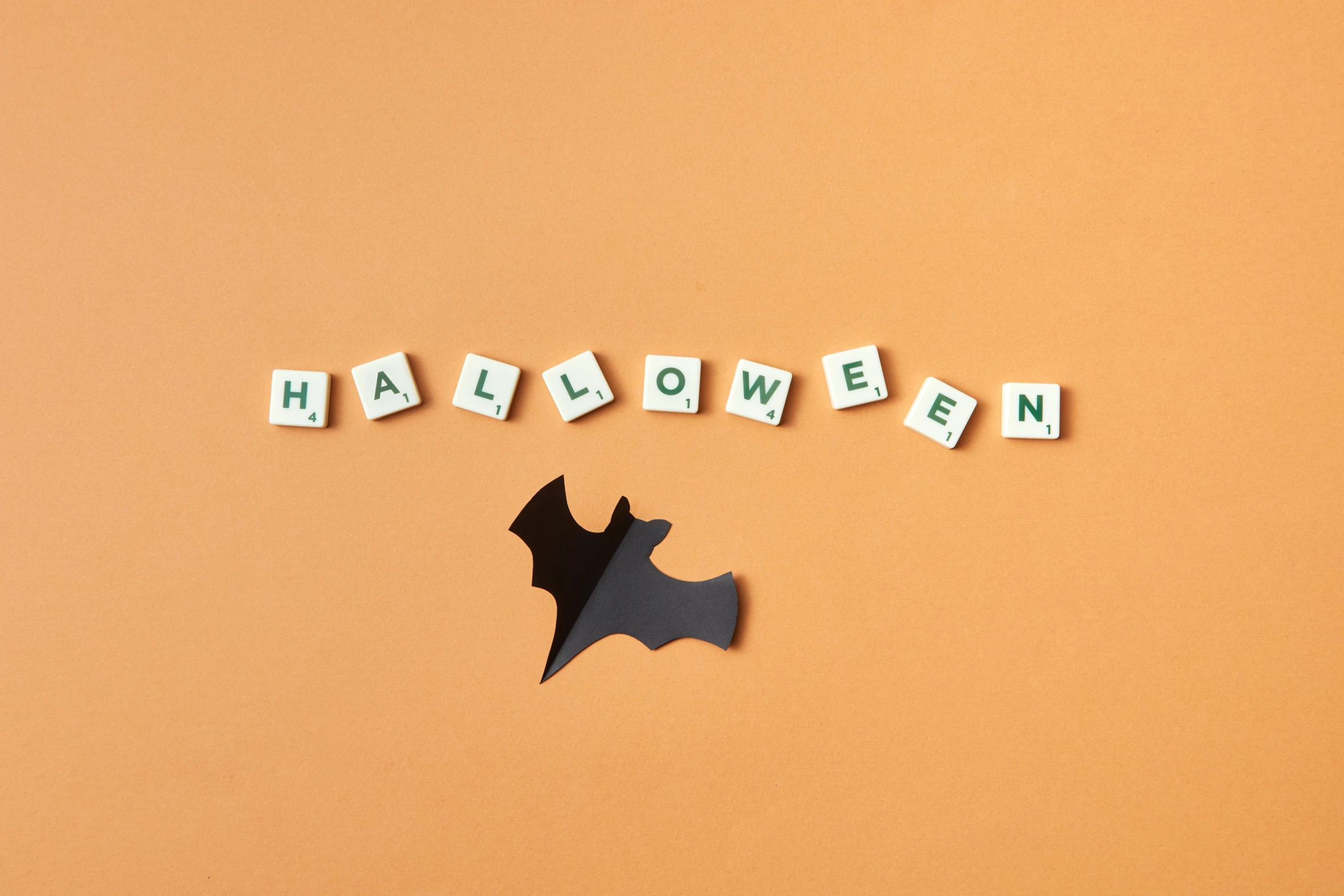 a bat is lying out of the word halloween spelled out of scrabble letters