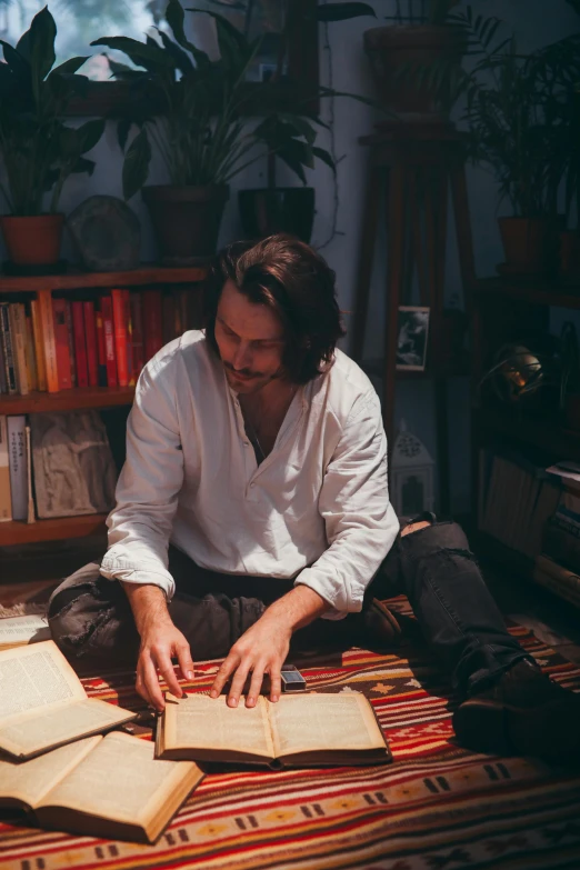 the man is sitting on a rug with several books on the ground