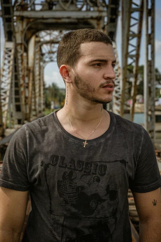 the man in black t - shirt poses in front of a bridge