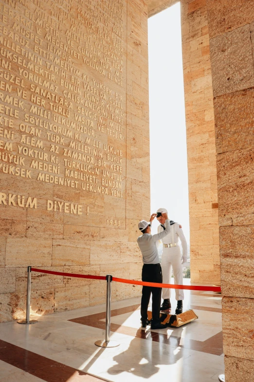 two men wearing suits and holding white towels in front of a building with names engraved on it