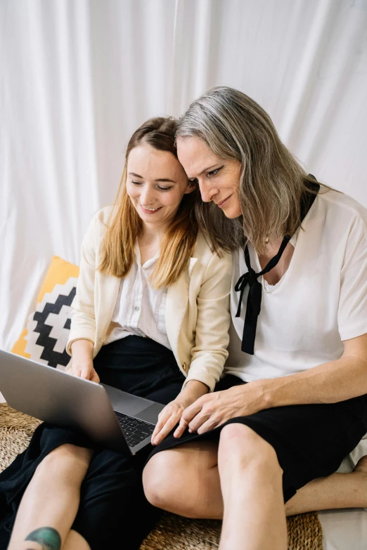 two women sitting together on the floor looking at a laptop