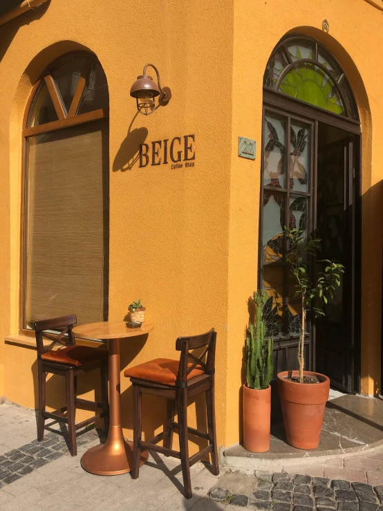 a yellow building with potted plants next to the sidewalk