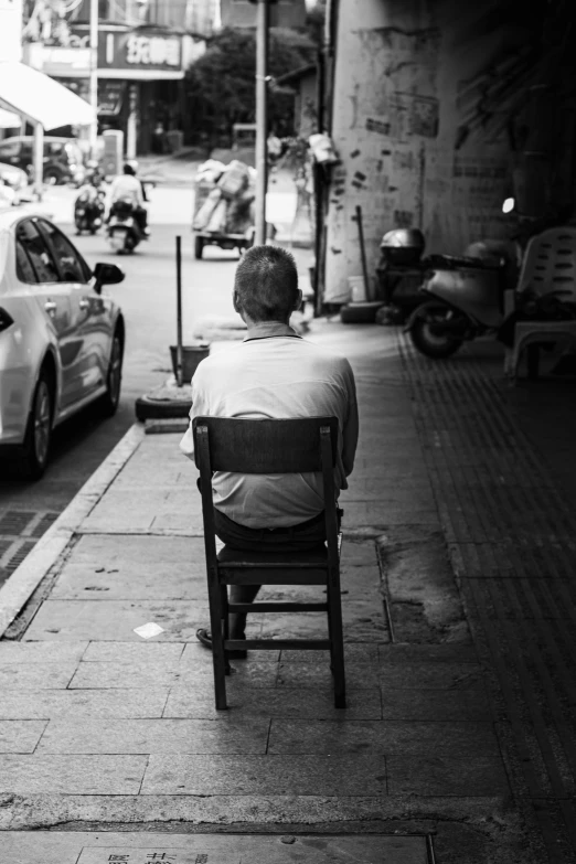 a person sitting in a chair on the sidewalk near some traffic