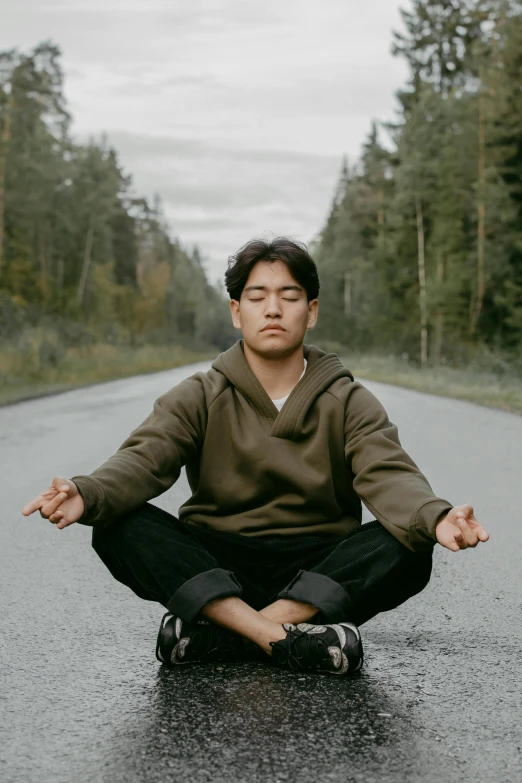 a young man sitting in the middle of a road doing yoga exercises