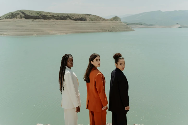 three women standing in front of a lake looking back at the camera