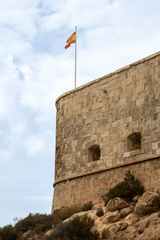 the flag of spain on top of a tower of a building
