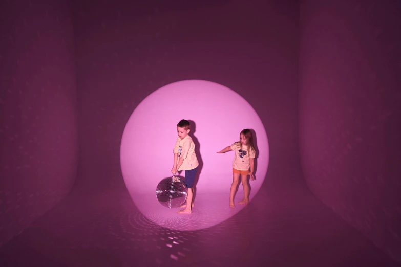 two young children stand inside a sphere while one person walks towards the camera