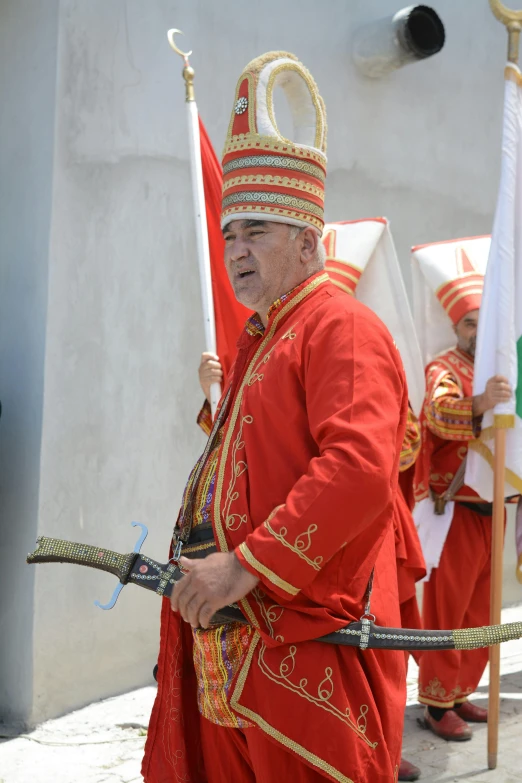 an older man in red and gold outfit holding two white flags