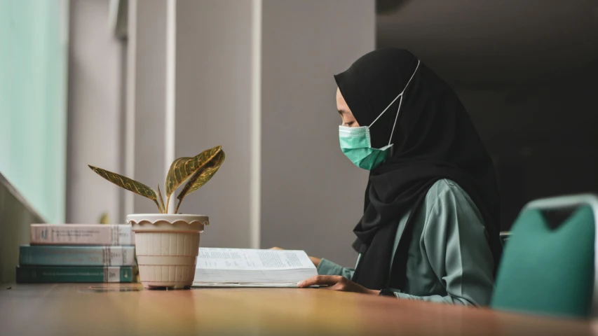 the woman wearing a mask is sitting down and reading a book