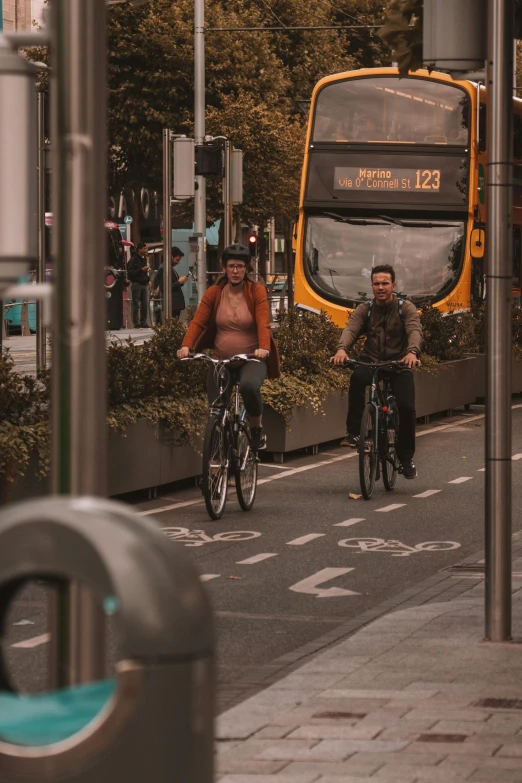 two men ride bikes on the street next to a yellow bus