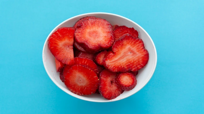 a small bowl of strawberries is displayed on a blue surface