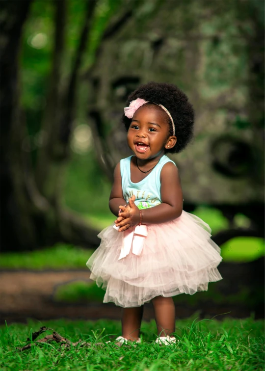 a young african girl stands in grass with a pink bow