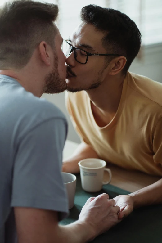 two men talking over coffee, one of them is biting into the other's mouth