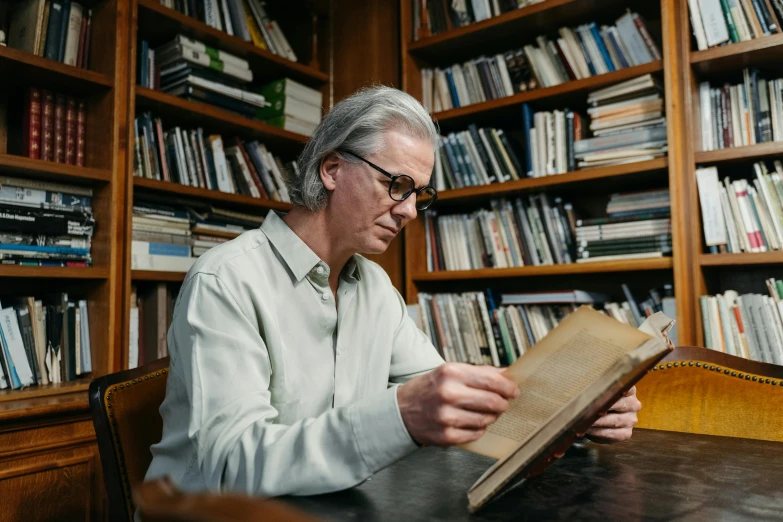 a man reading a book in front of bookshelves