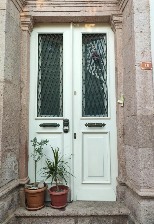 potted plants outside an old, white door on the sidewalk