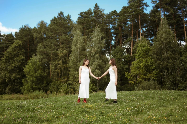 two people in white dresses hold hands while standing near trees