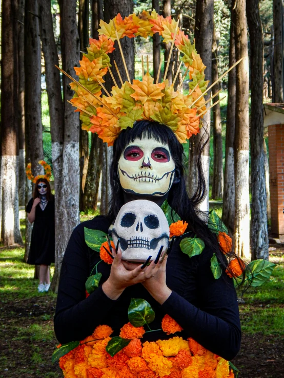 a person with skeleton face paint holding up a skull in front of some trees