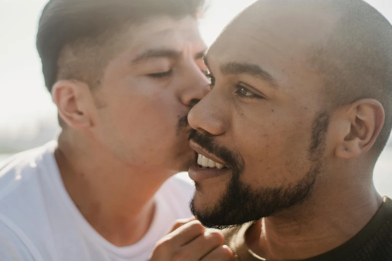 one male looking down while another male is kissing him