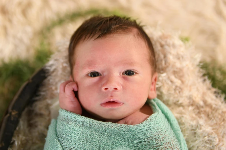 a newborn baby wrapped in green laying on a white blanket