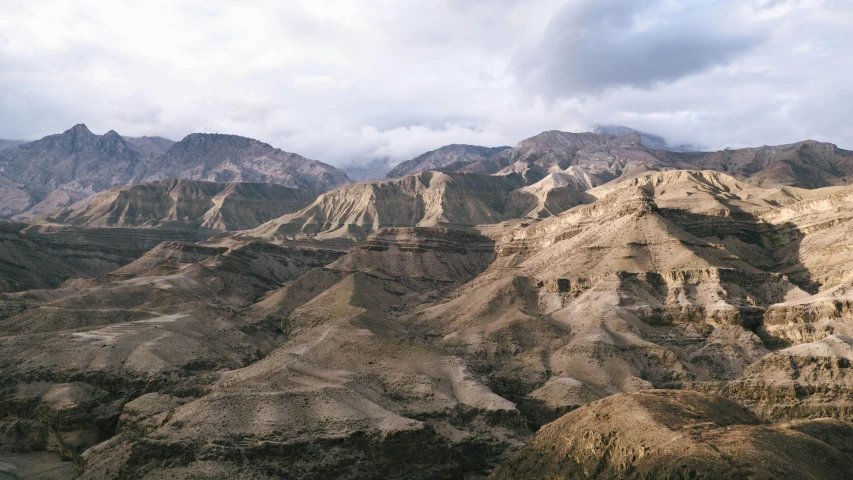 a mountain range in the distance is surrounded by brown mountain and green fields