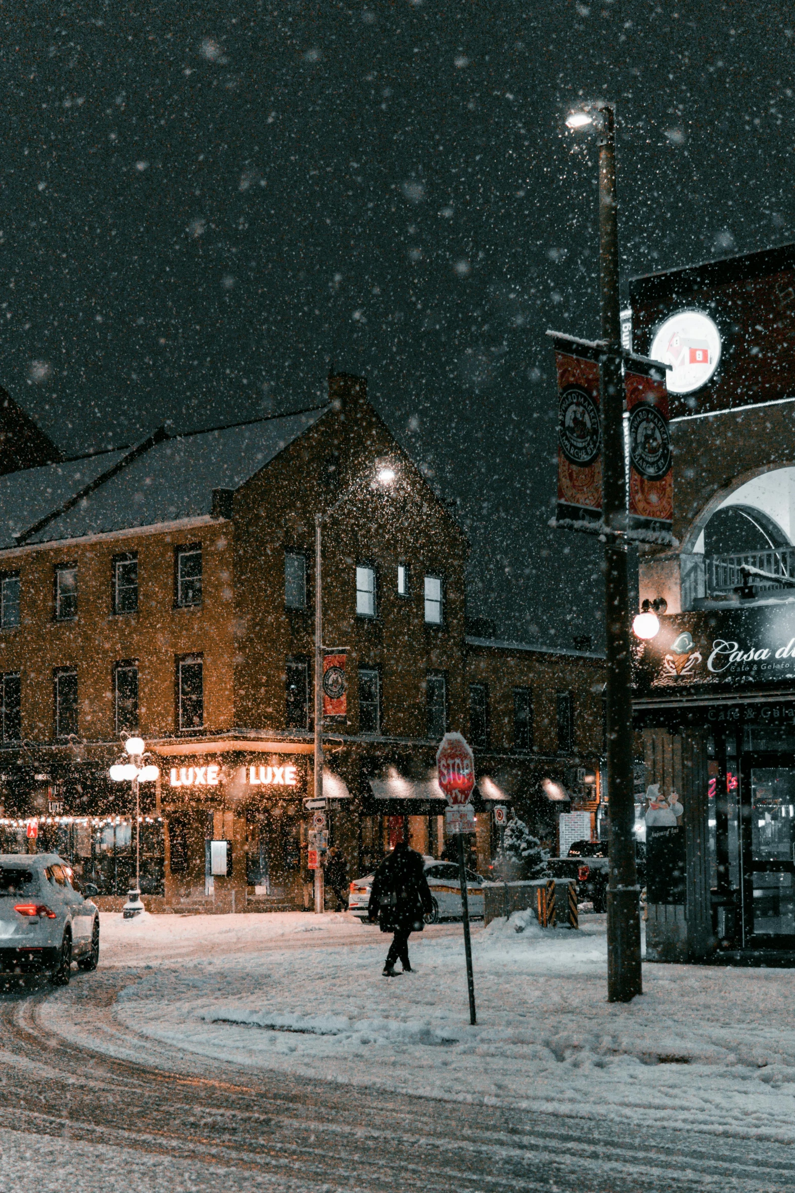 a snow - covered town at night with people walking and car parked on the side