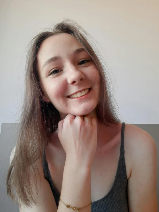 smiling woman in tank top leaning up against white wall